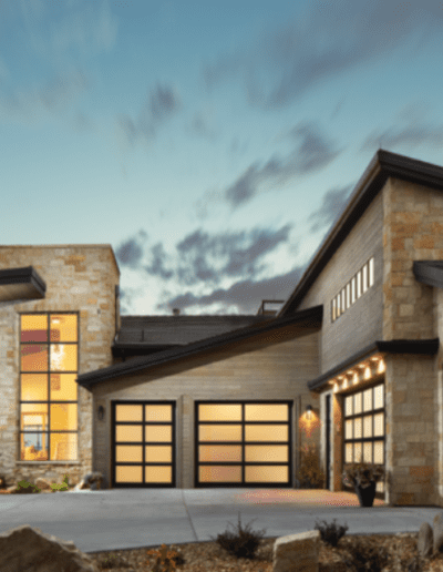 Modern single-story house with illuminated windows and a stone facade at twilight.